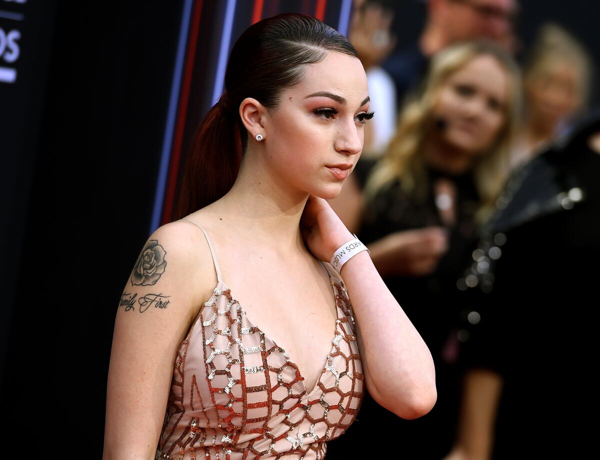Bhad Bhabie wearing a formal gown and a wristband with her hair swept back and holding her hand to her neck.