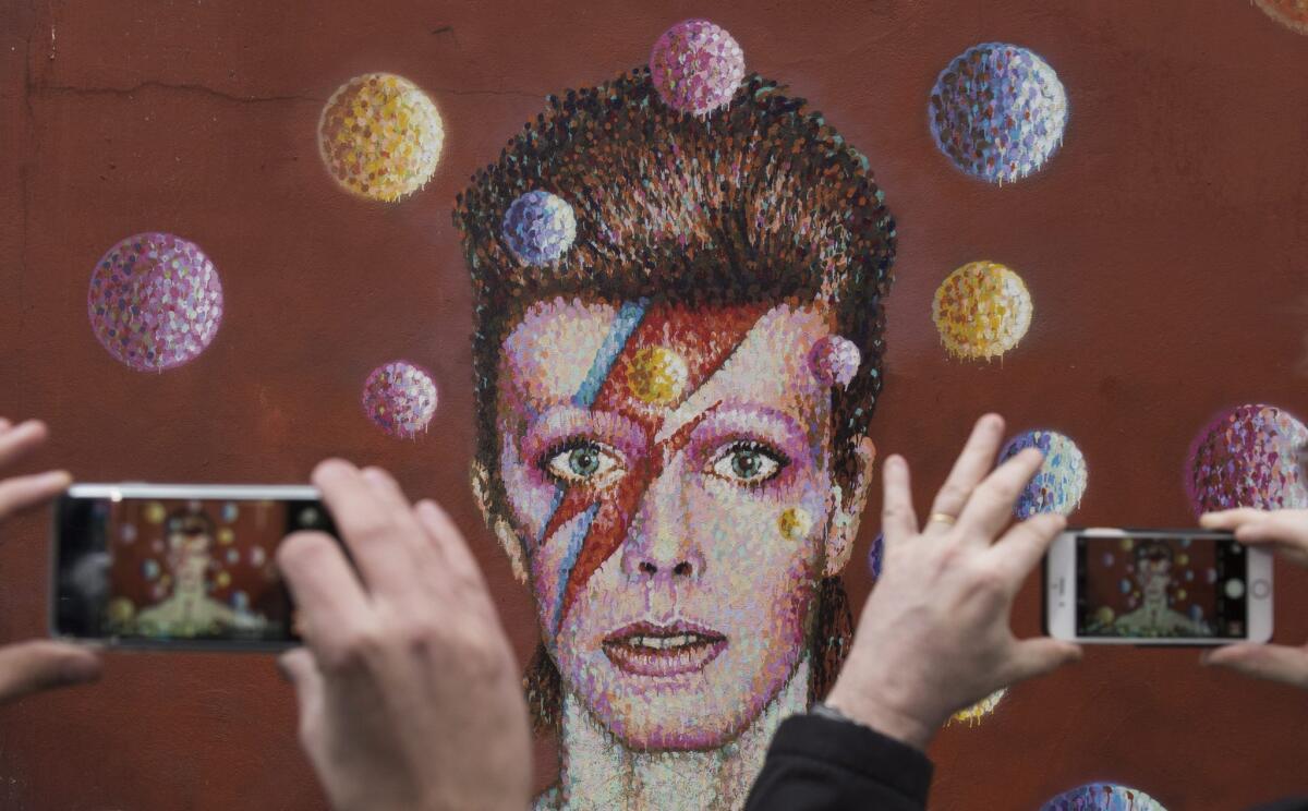 People take photographs of a mural of David Bowie in the London district of Brixton, where the British singer was born. Bowie died Sunday at age 69.