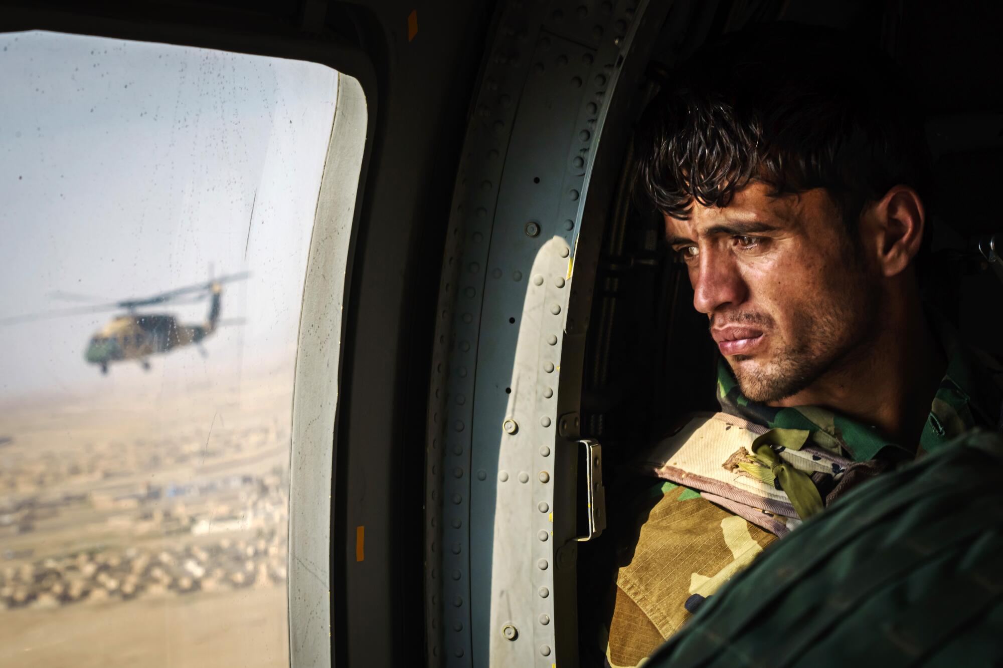 A weary-looking soldier looks out the window of a helicopter