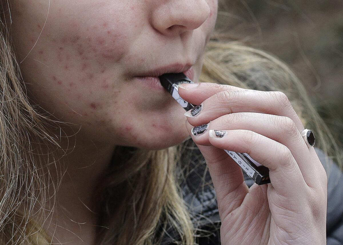 A high school student uses a vaping device near a school campus in Cambridge, Mass. 