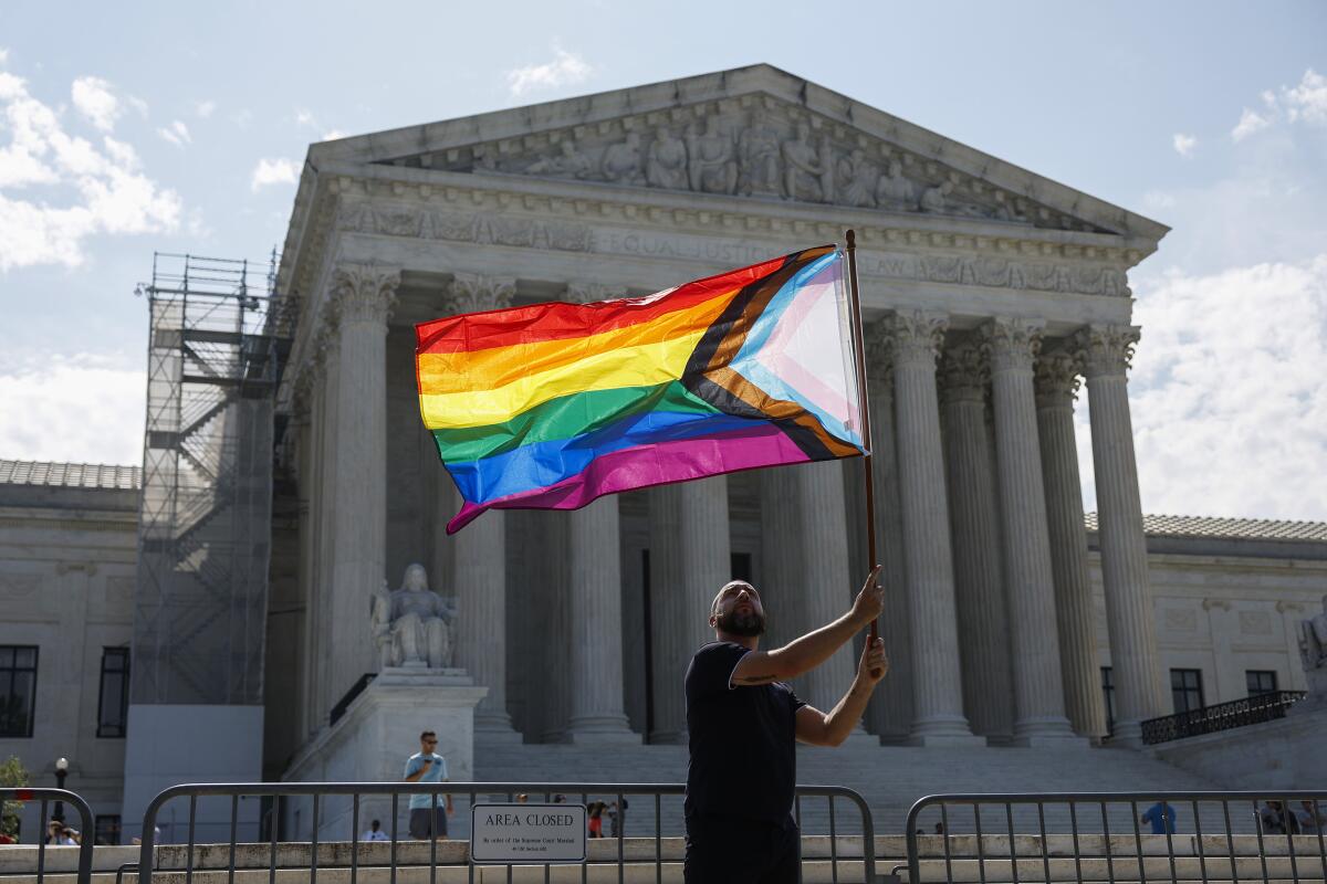 A man holds up a LGBTQIA pride flag in the breeze in front of the Supreme Court building.