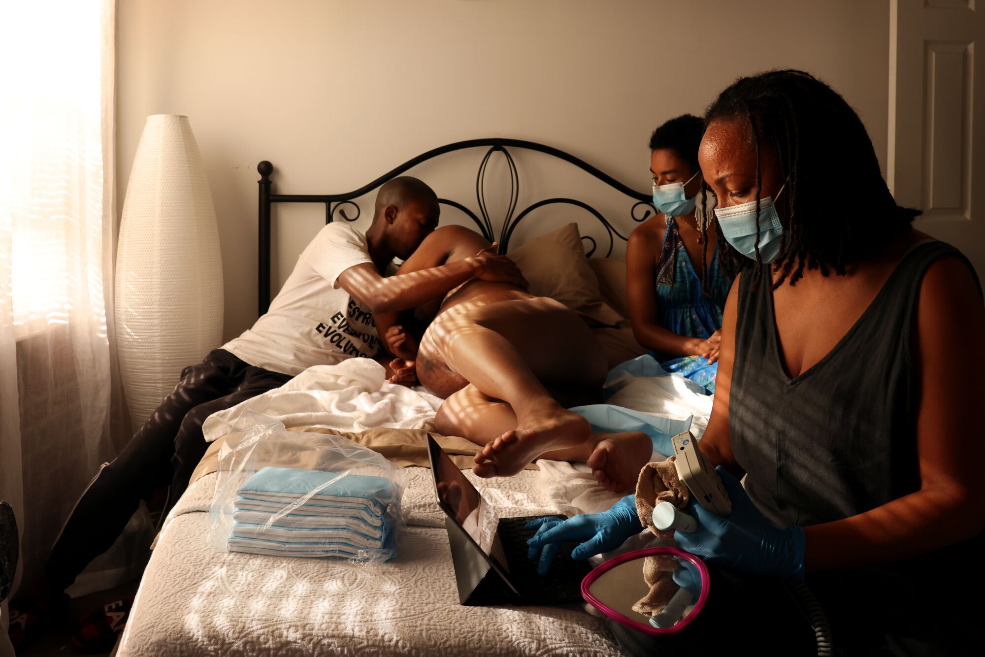 A woman in labor is comforted by her husband in a bed, alongside two other women