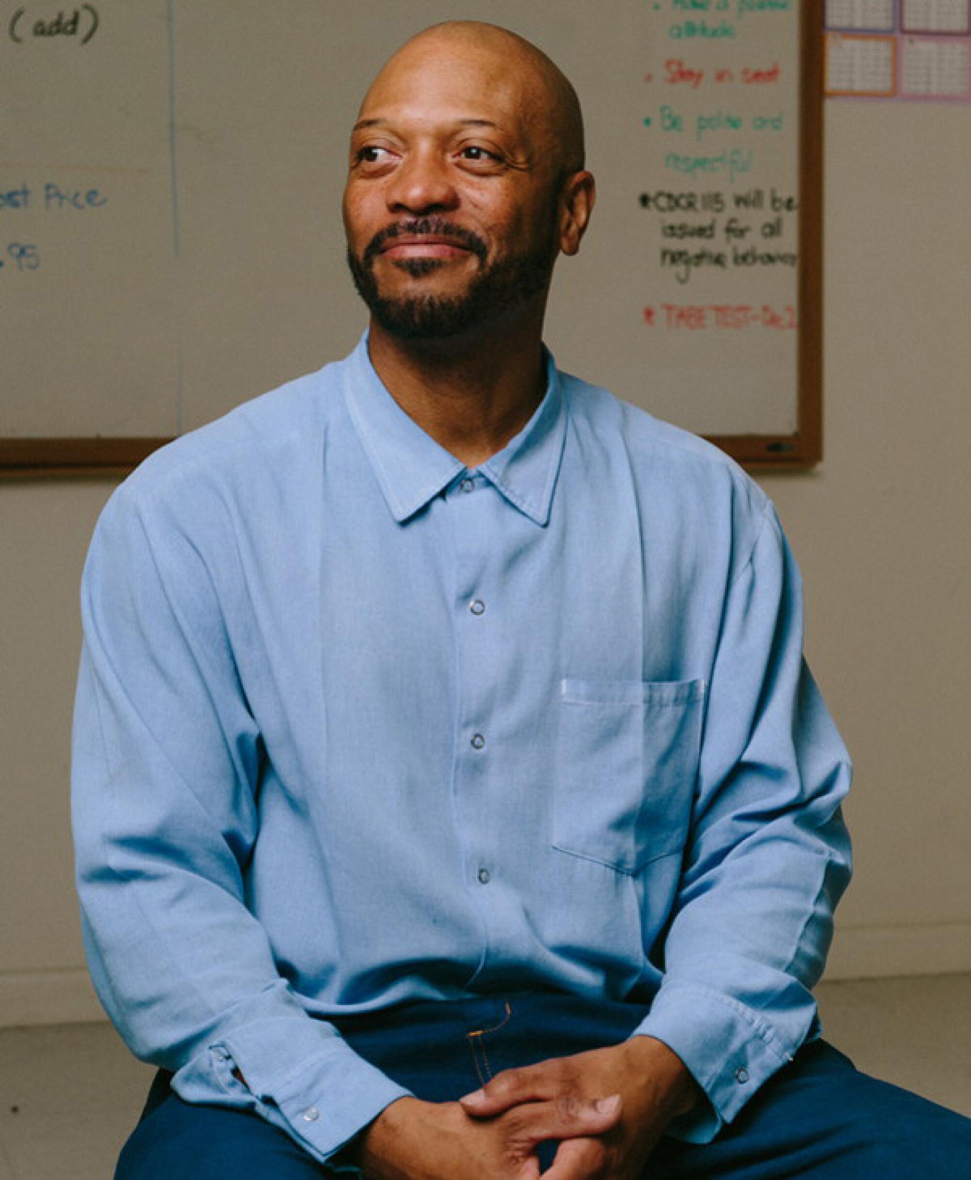 A smiling man in his 40s wearing a blue button-up shirt sitting in a classroom