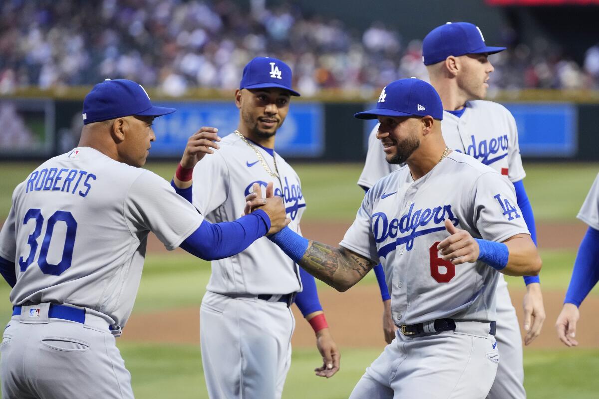 Dodgers manager Dave Roberts, left, shakes hands with outfielder David Peralta in front of right fielder Mookie Betts.