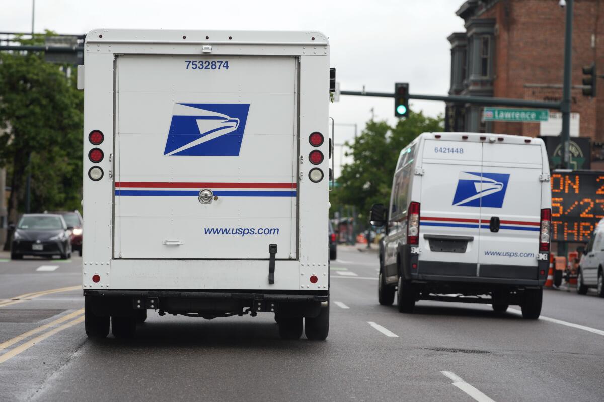 ARCHIVO - Dos vehículos del Servicio Postal de Estados Unidos avanzan por una calle de Denver 