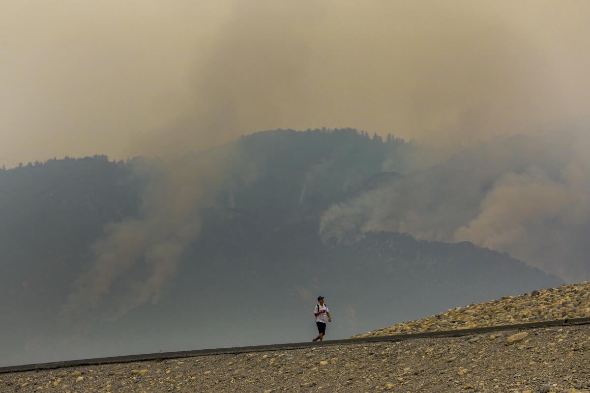A man walks on Santa Fe Dam as smoke rises from Bobcat fire in the San Gabriel Mountains above Duarte.