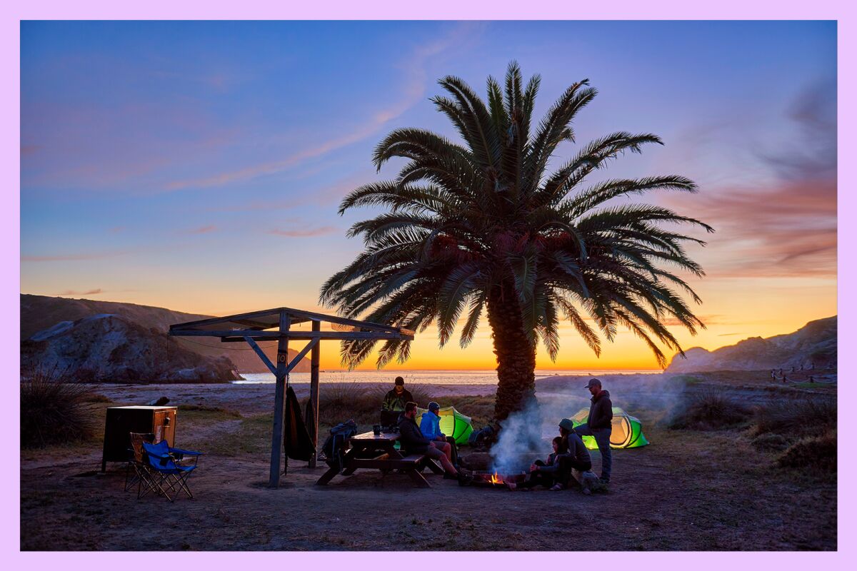 A group of folks camp on a beach during sunset.