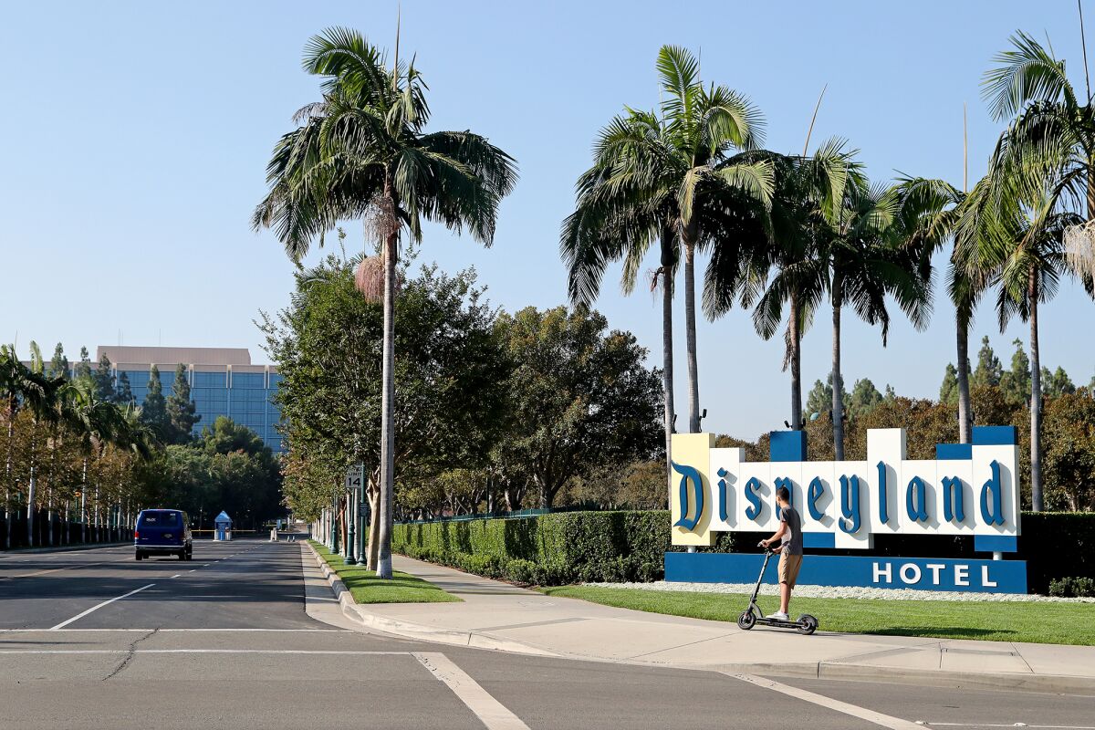 A person on a scooter cruises by the Disneyland Hotel sign.