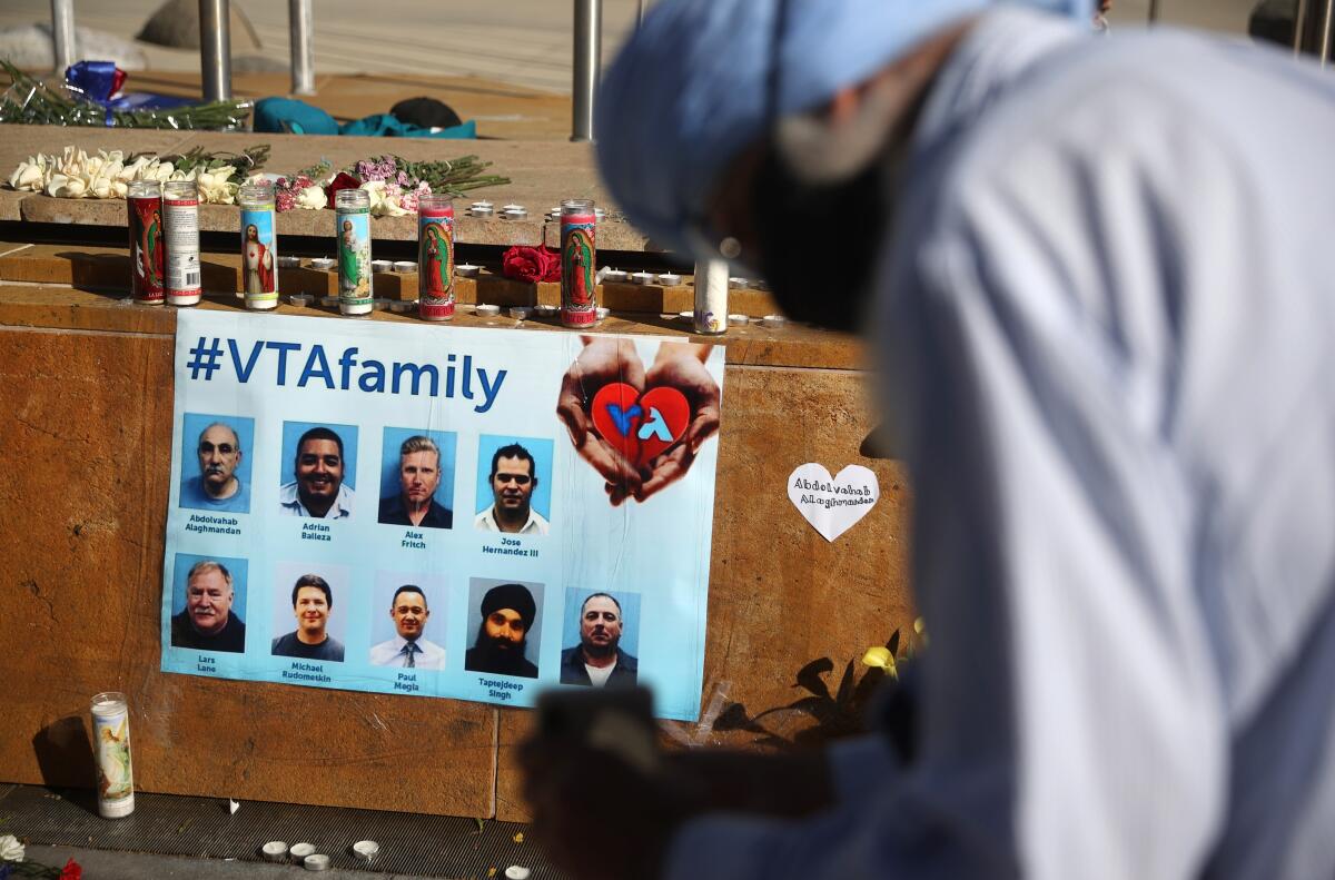 A person bows their head in front of candles, flowers and a sign with photos of nine people and the hashtag VTA family