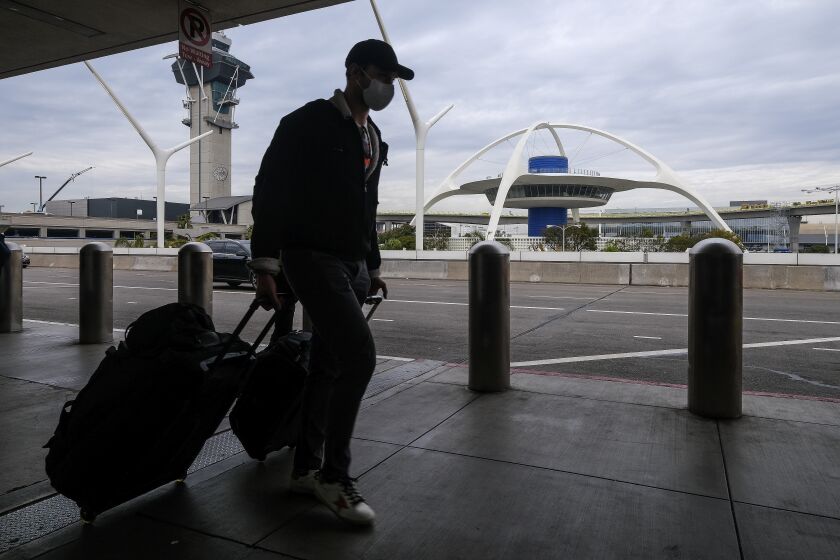 A holiday traveler wearing a face mask arrives at the Los Angeles International Airport in Los Angeles, Wednesday, Dec. 22, 2021. (AP Photo/Ringo H.W. Chiu)