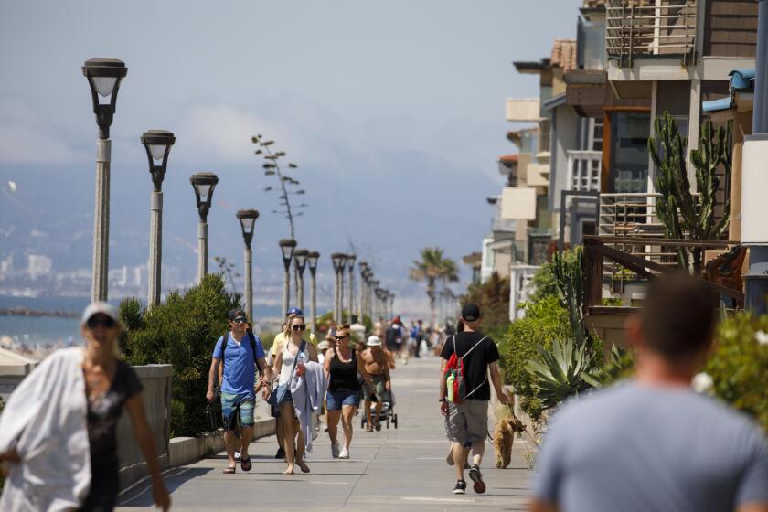 People walk dogs past beachfront homes on The Strand north of the pier on Sunday, August 18, 2019 in Manhattan Beach, CA. (Patrick T. Fallon/ For The Los Angeles Times)