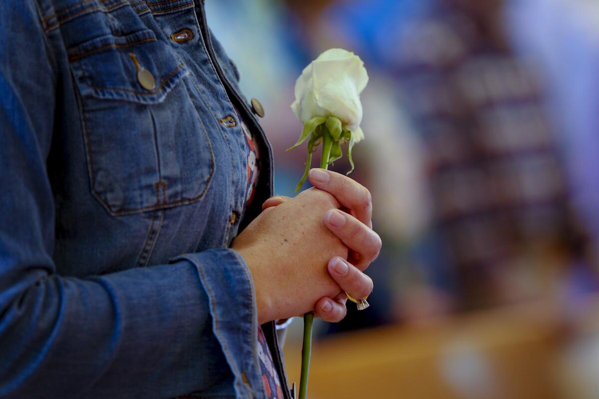 A parishioner holds a single white rose at mass for survivors of Suicide