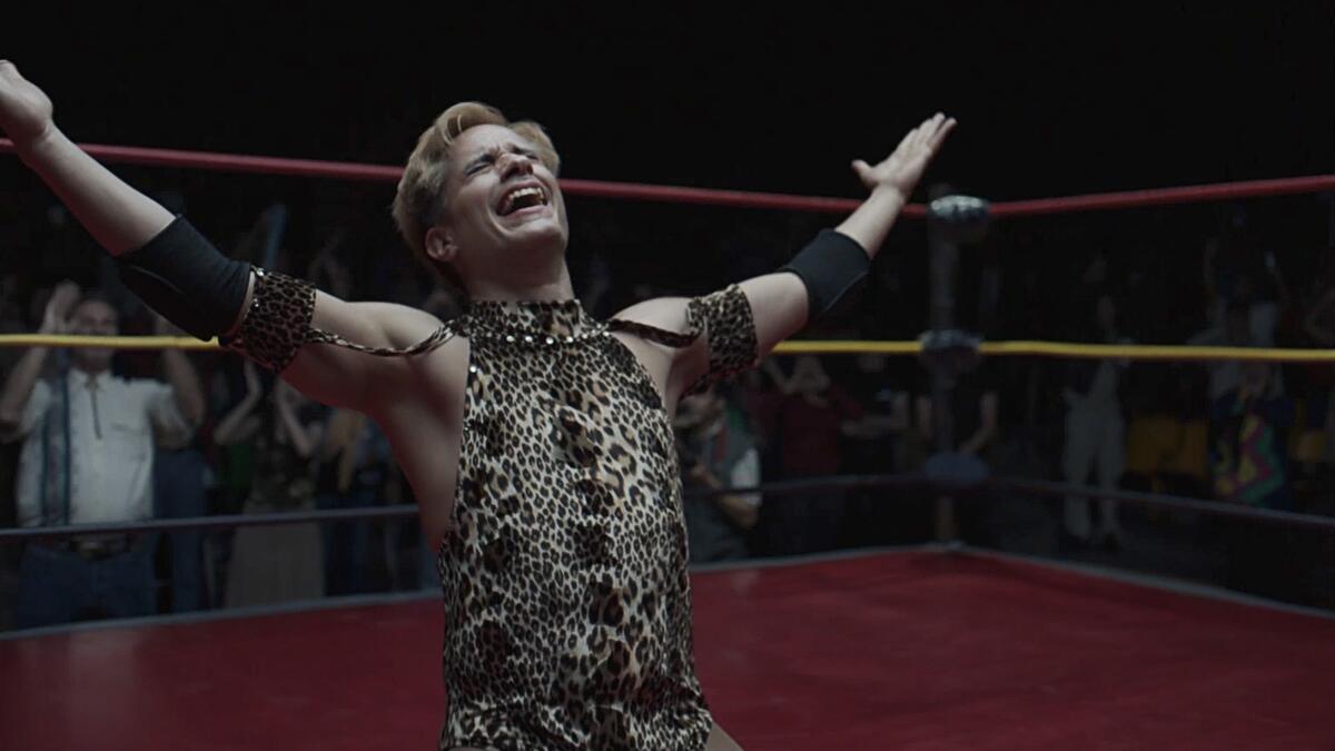 A wrestler exults in a moment of triumph with arms raised while he kneels in a ring.