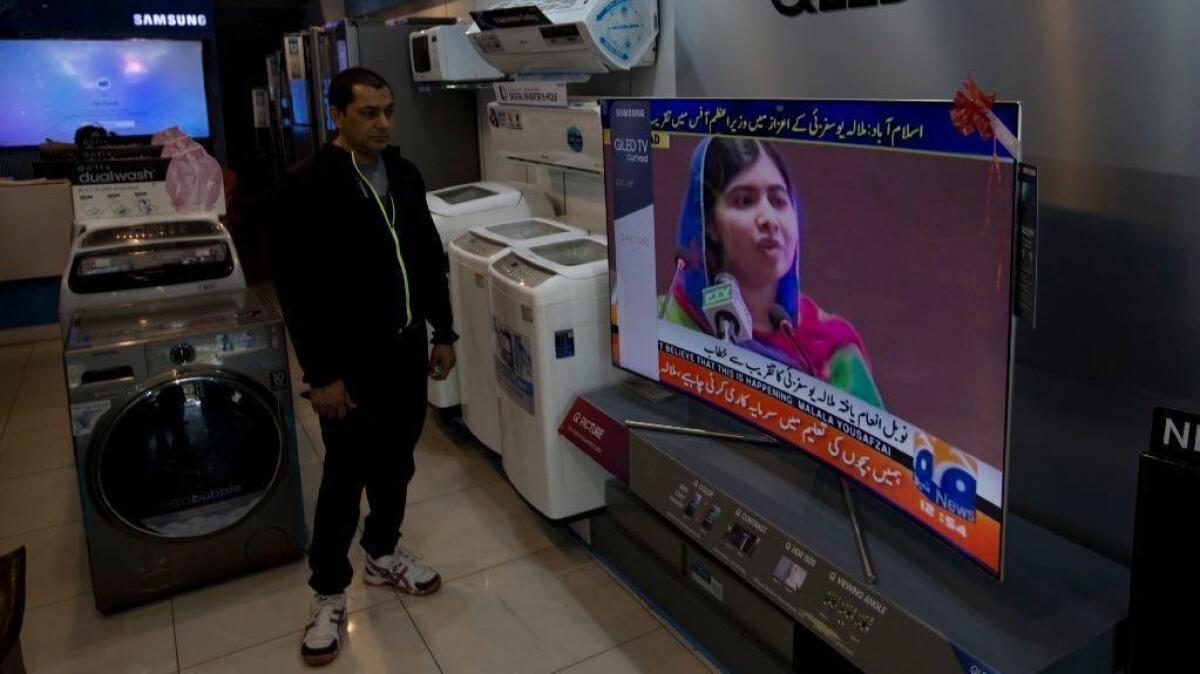A Pakistani shopkeeper listens to Malala Yousafzai addressing a reception in Islamabad, the capital.