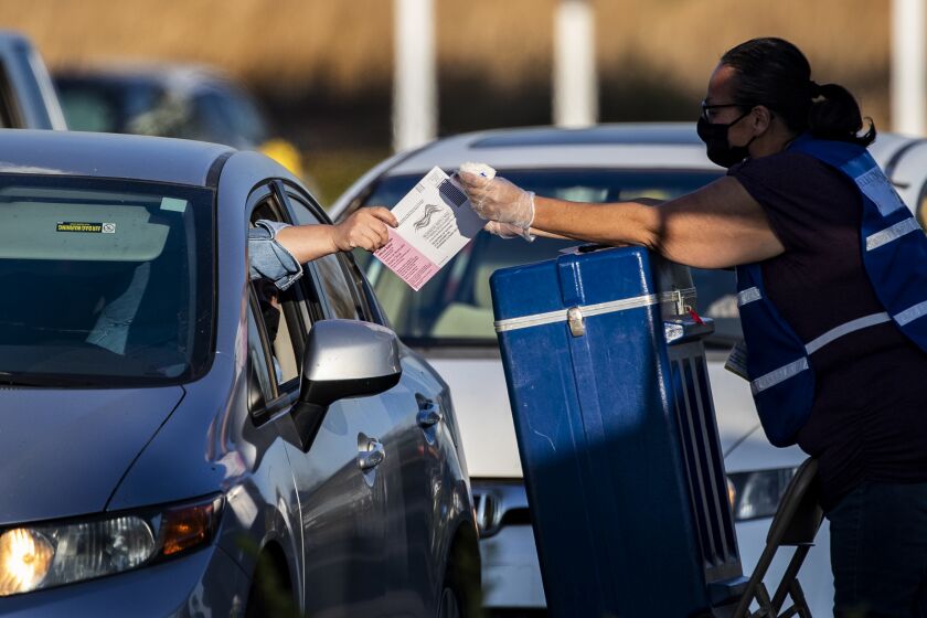 RIVERSIDE, CA - OCTOBER 30, 2020: A voter hands her ballot to an election official to be dropped in a ballot box during a drive-thru ballot drop-off at the Registrar of Voters Office on October 30, 2020 in Riverside, California. There was a steady line of cars up until the 5pm closing time.(Gina Ferazzi / Los Angeles Times)