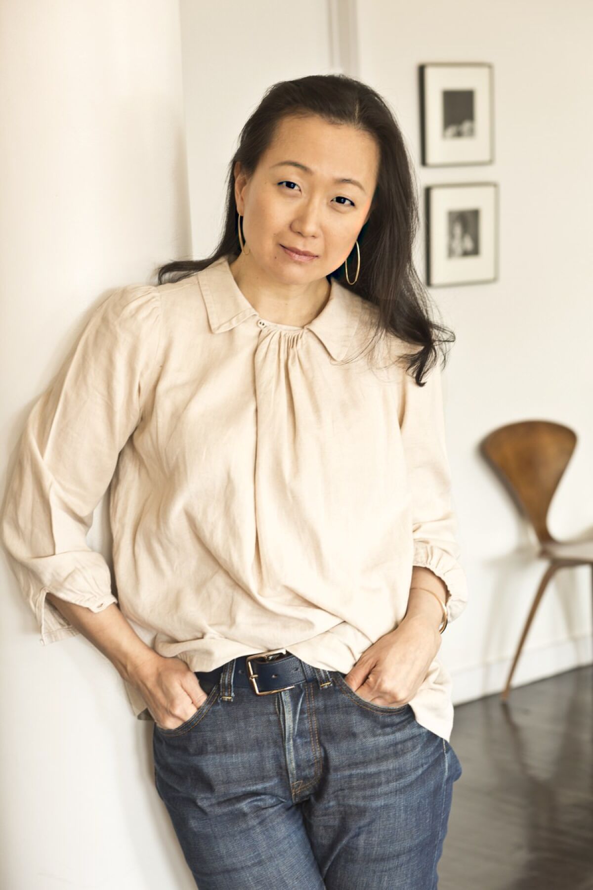A woman leaning against a wall with her hands in her pants pockets