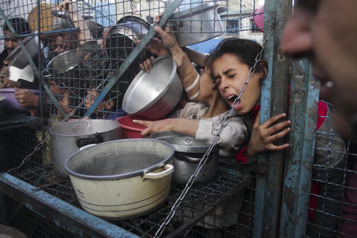 Palestinians press against a fence, trying to get food placed in their cooking pots at a refugee camp in Gaza.