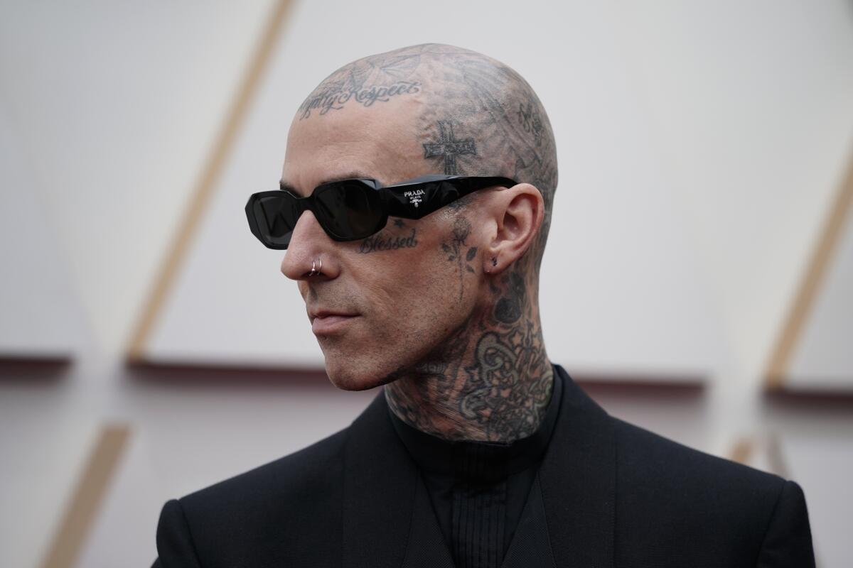 A bald tattooed man wearing sunglasses and a black suit poses for red carpet photos. 