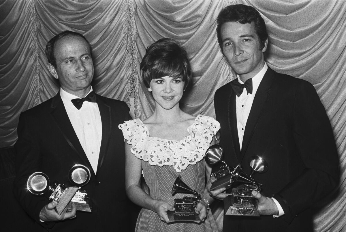 A black and white photo of two men flanking one women, all three holding Grammy Awards