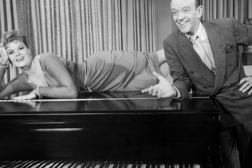 ca.0414.stockings4.Janis Paige as Peggy Dayton lying across the top of a grand piano and Fred Astaire as Steve Canfield leaning against the piano, hand on hip, performing musical number "Stereophonic Sound.", in Warner Bros. COLE PORTER MUSICAL movie, "Silk Stockings" 1957.