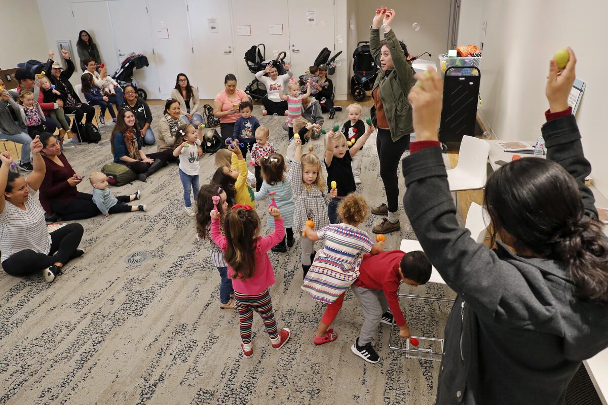 Librarians Liana Lujan, top right, and Rosalba Rivera, bottom right, encourage visitors to shake maracas as they listen to stories and sing songs in English and Spanish during Bilingual Storytime at the Donald Dungan Library in Costa Mesa on Thursday.