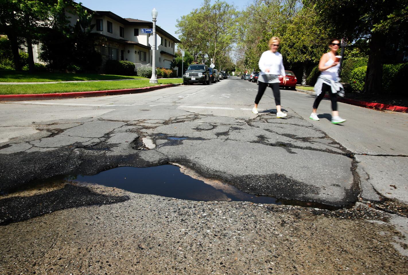 Pedestrians walk near a pothole in need of repair at the intersection of McCadden Place and 4th Street in the Hancock Park area of Los Angeles.