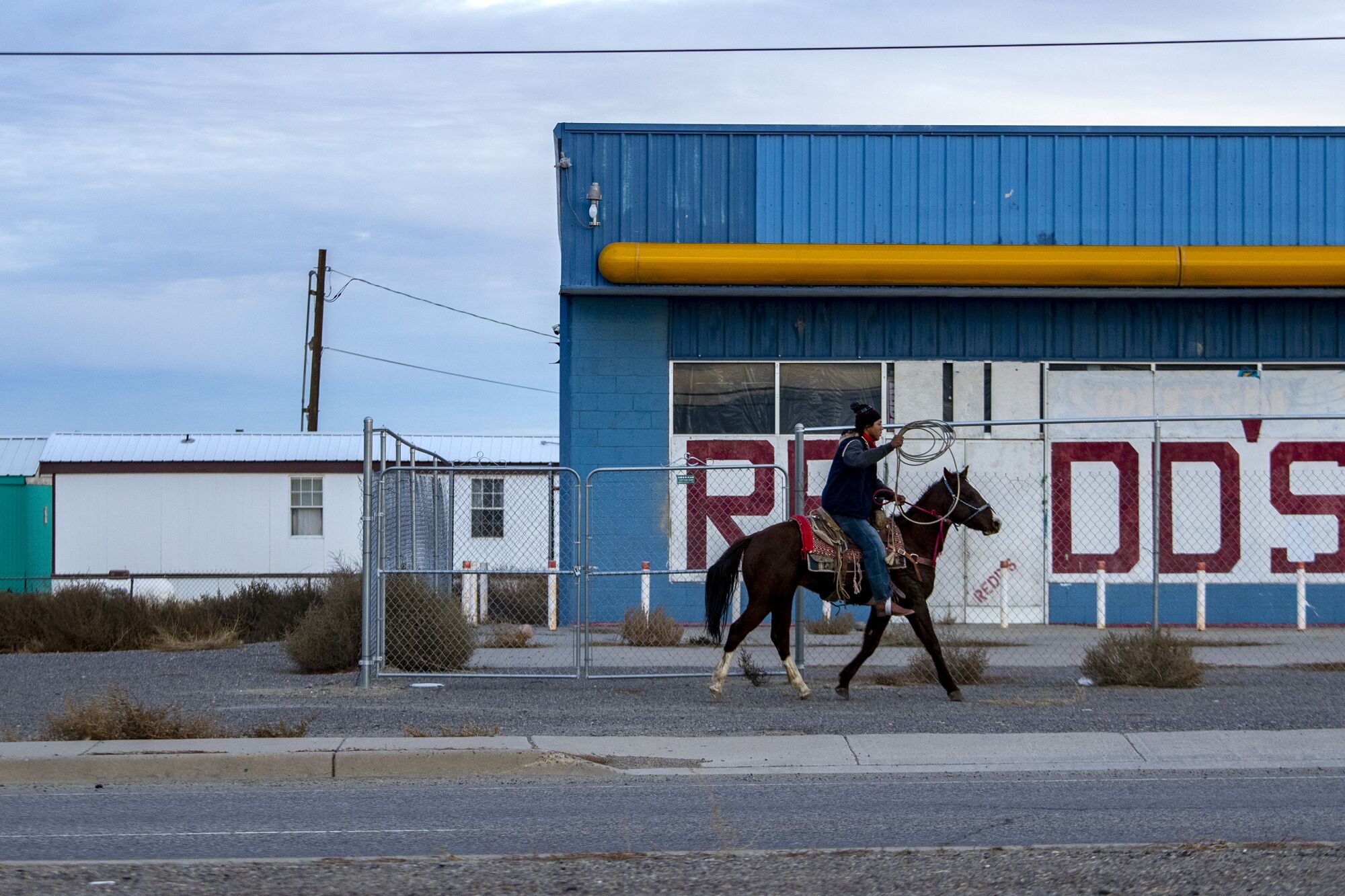 A man carrying a rope rides through a town on a horse in Navajo Nation.  