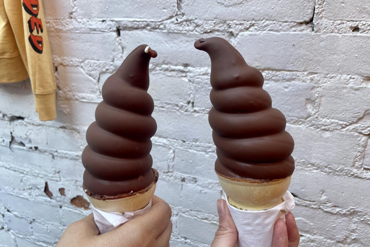 Hands hold up two chocolate-dipped soft serve cones from Heavy Handed.