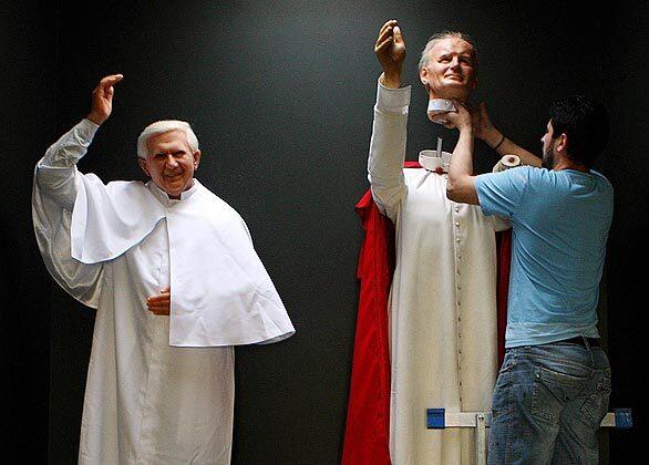 Danny Balan lifts up the waxwork head of Pope John Paul II into place beside the waxwork of Pope Pope Benedict XVI during final preparations for the official reopening of the National Wax Museum Plus on Wednesday.