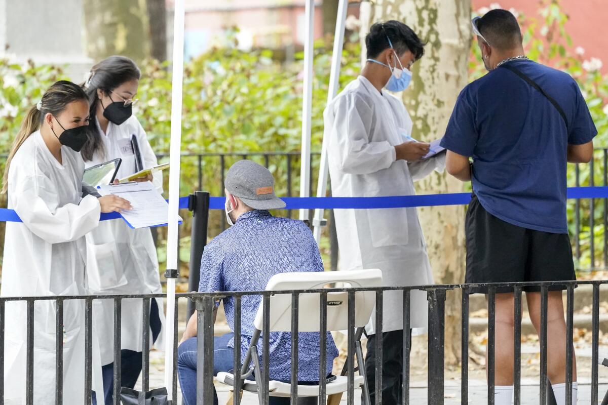 Masked healthcare workers handing clipboards to people waiting in line outdoors