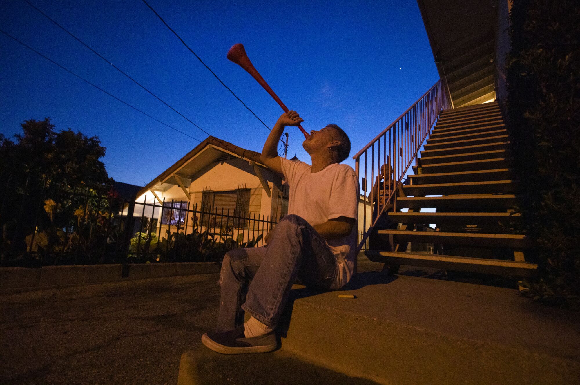 Booka Bickar, 59, makes noise with a plastic horn outside a friend's apartment on Lucile Ave. in Silver Lake, drawing attention to thank essential workers and all the people on the front lines against the coronavirus. Every night for about 5 minutes, starting at 8pm sharp, he and other people on the block and the surrounding area make noise thanking workers.