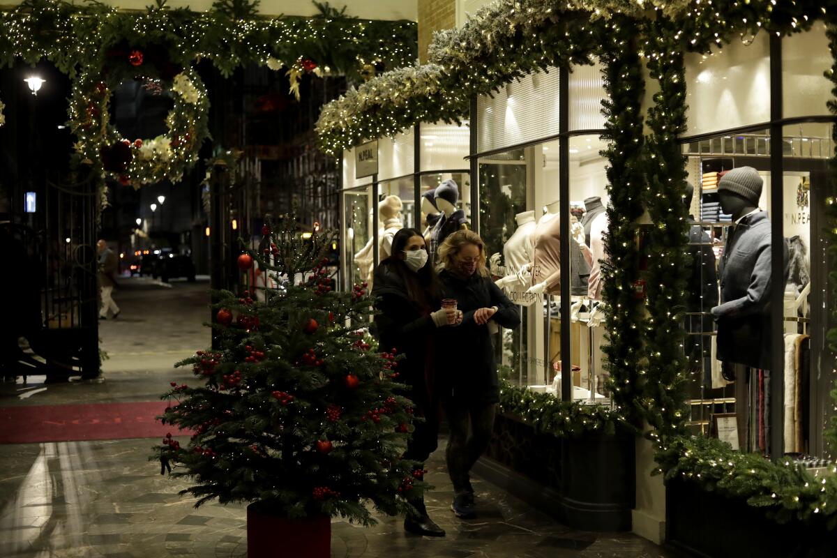 Unas mujeres con cubrebocas por el coronavirus pasan frente a una tienda de ropa en Burlington Arcade, Londres.