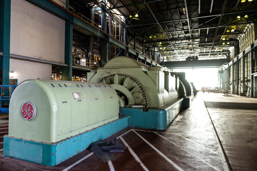 A long piece of machinery inside a power plant that's mostly open to the outside. At one end it has a prominent GE logo.