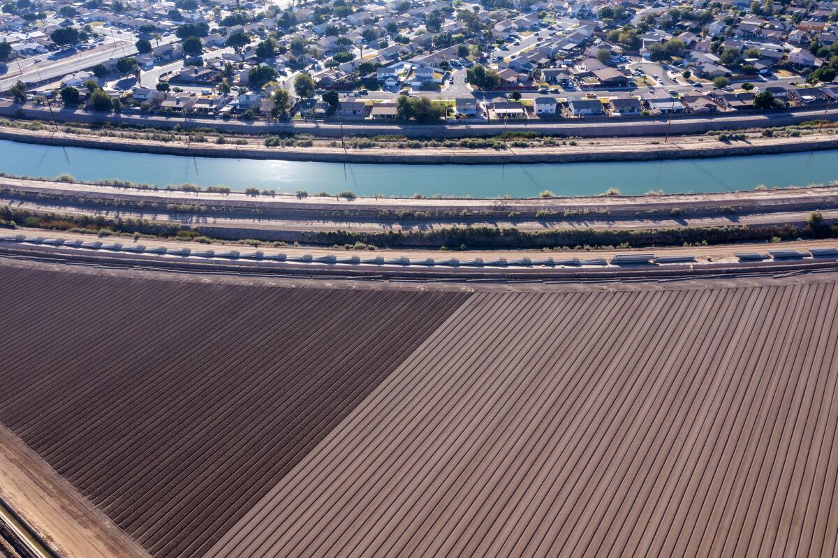 A canal carries water past farmland and a suburban development.