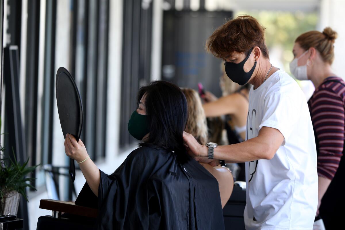 Travis Vu, 47, of Anaheim, finishes cutting the hair of client Thuy Ngo outside TravisVu The Salon on Aug. 1.