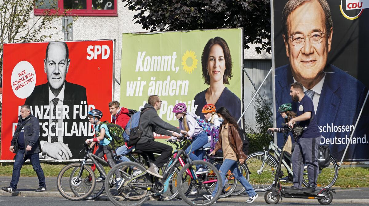 People walk, bicycle and scooter past posters.