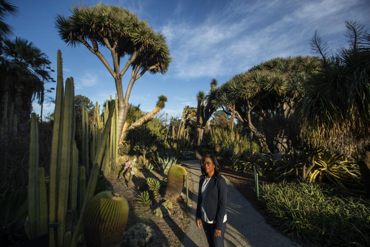 Misty Bennett, wearing a dark suit, stand on path surrounded by succulents in the Huntington's gardens
