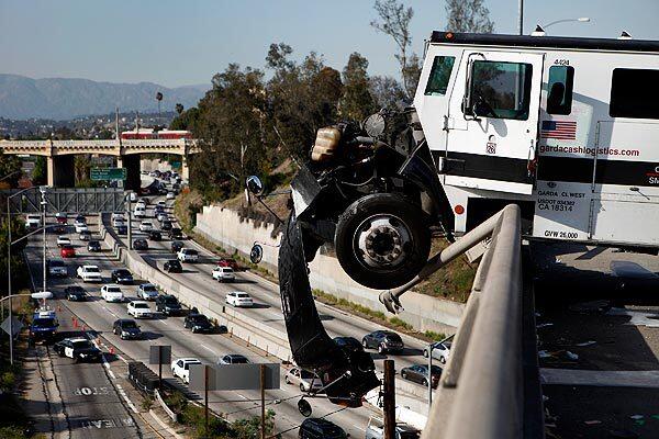 The front end of an armored car dangles over the guardrail of the I-5 freeway, at the I-10 transition, above 7th Street near downtown Los Angeles.