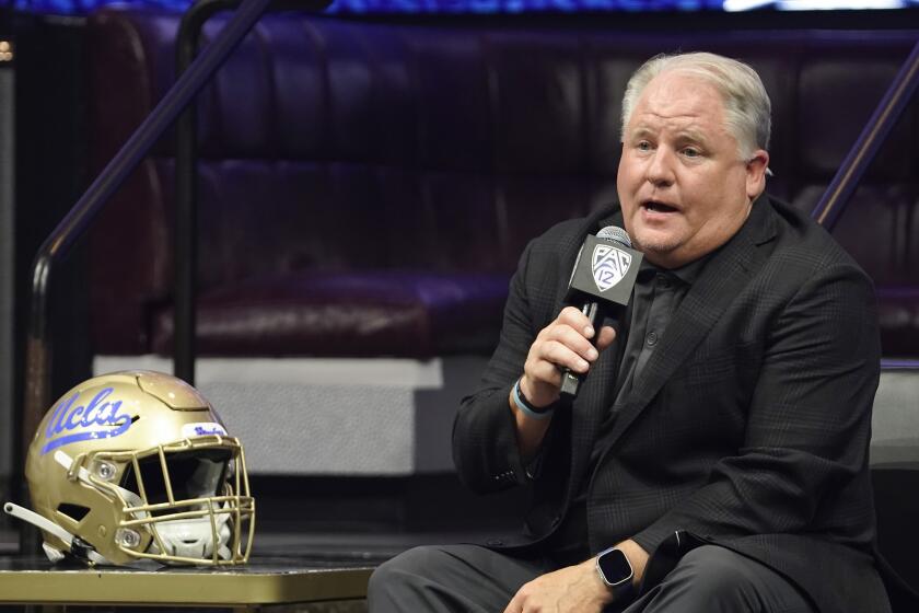 UCLA coach Chip Kelly holds a microphone and speaks at Pac-12 media day
