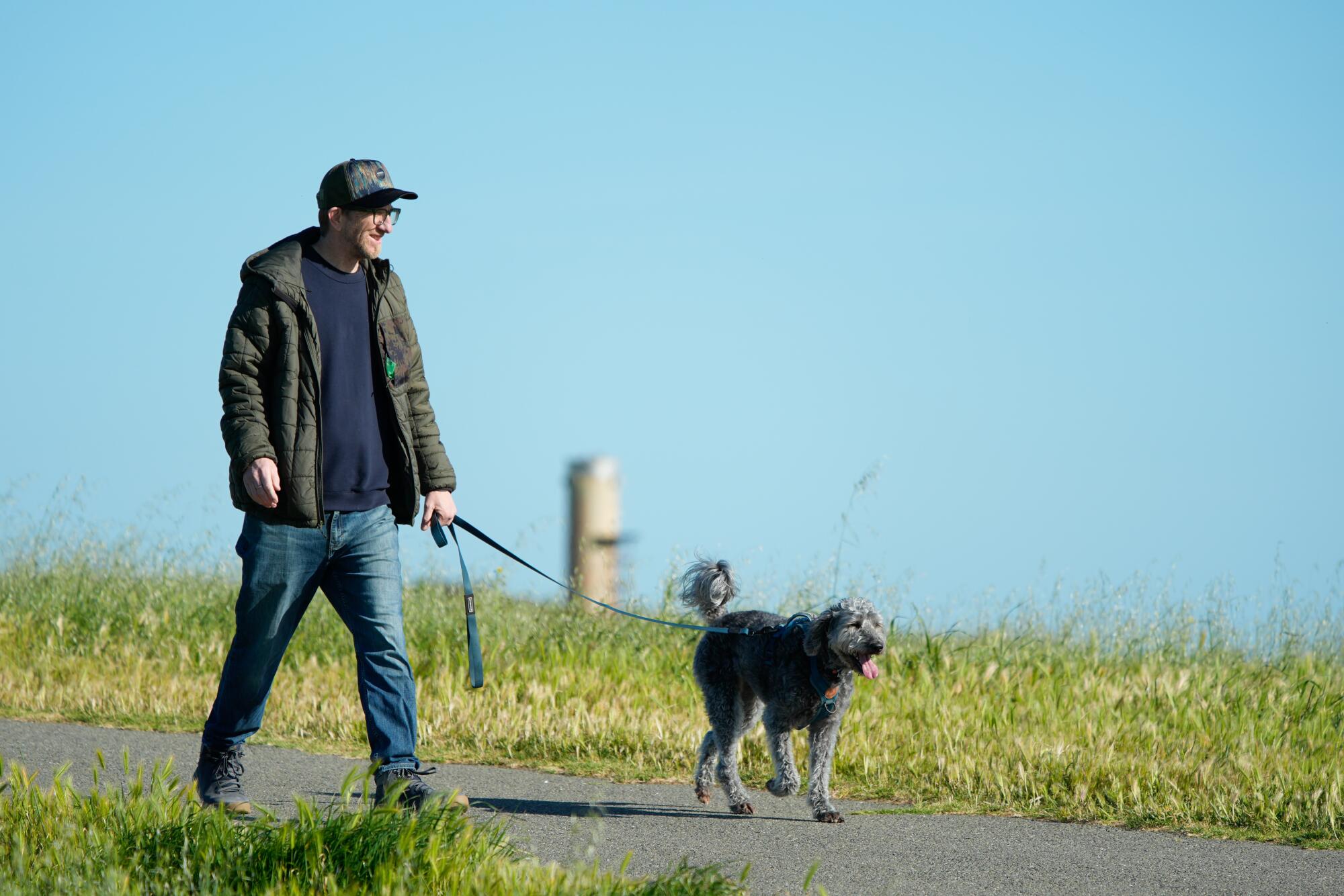 A man walks a dog along a grassy pathway 