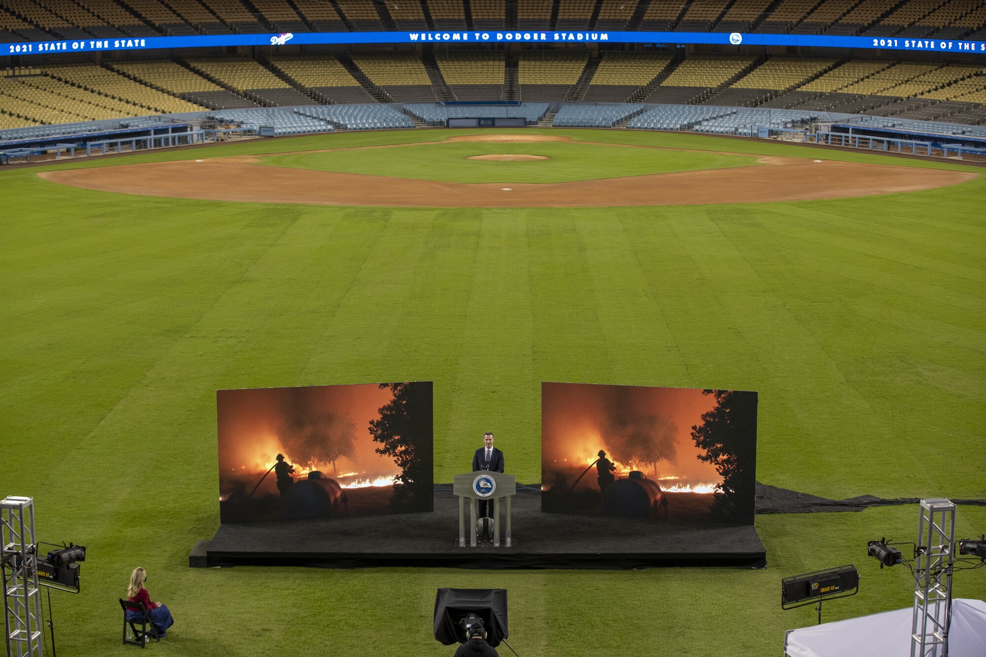 Two people and two large video screens are seen on a baseball field.