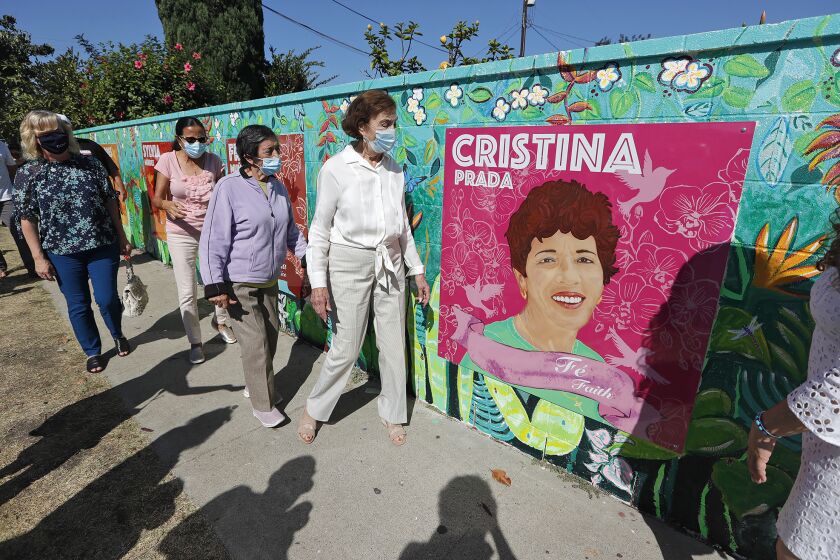 Honorees Cristina Prada and Frances Munoz, from left, next to artwork, walk past Prada's mural panel during during "Poderosas" mural dedication and unveiling ceremony in Costa Mesa on Monday. Munoz is included in one of the panel paintings that includes the likeness and of each woman's story and connection to California.