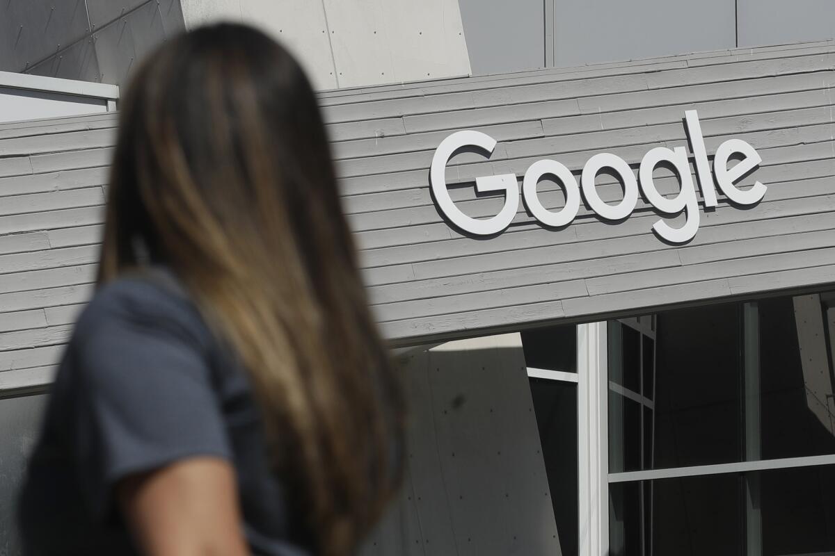 A person with long dark hair, seen from the side, is looking at a Google sign that has white letters on a gray background.