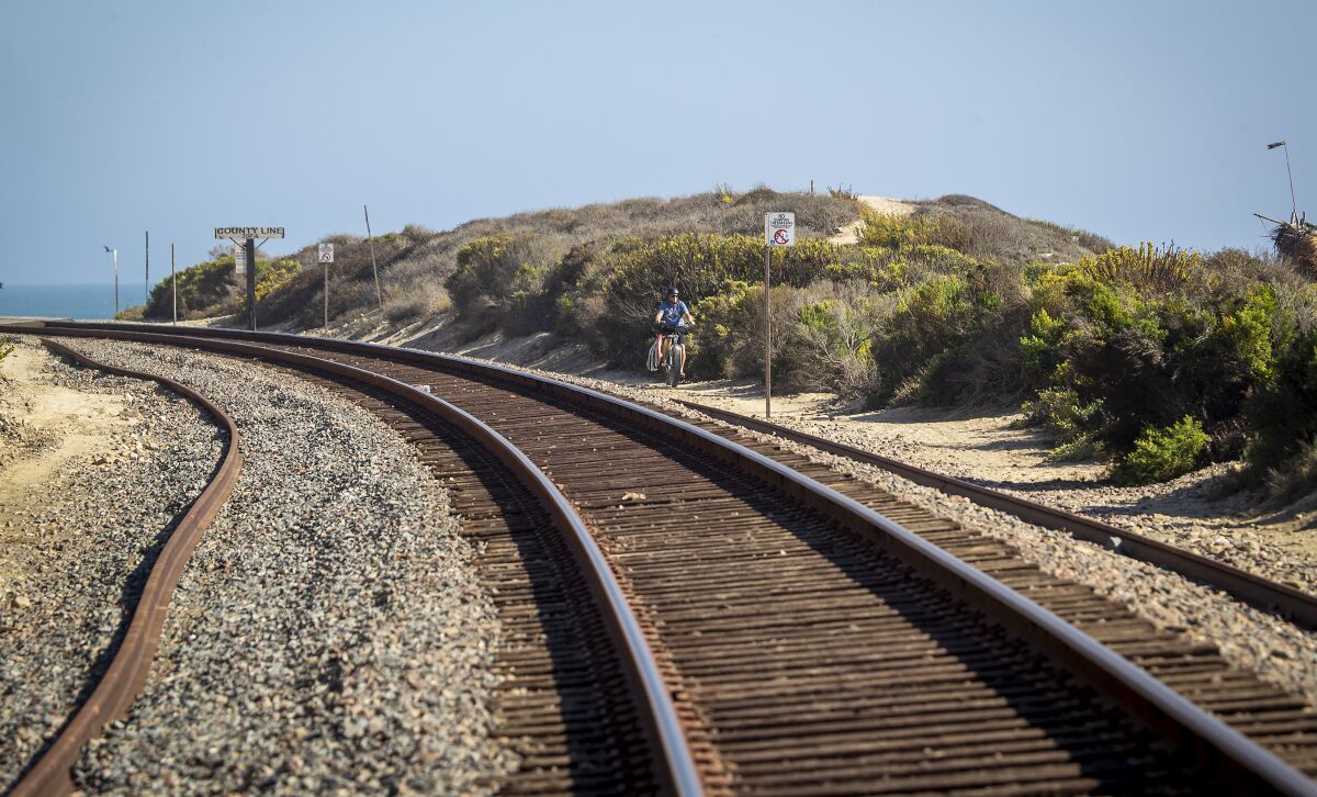 A surfer rides a bike along the closed tracks to surf Cotton's Point
