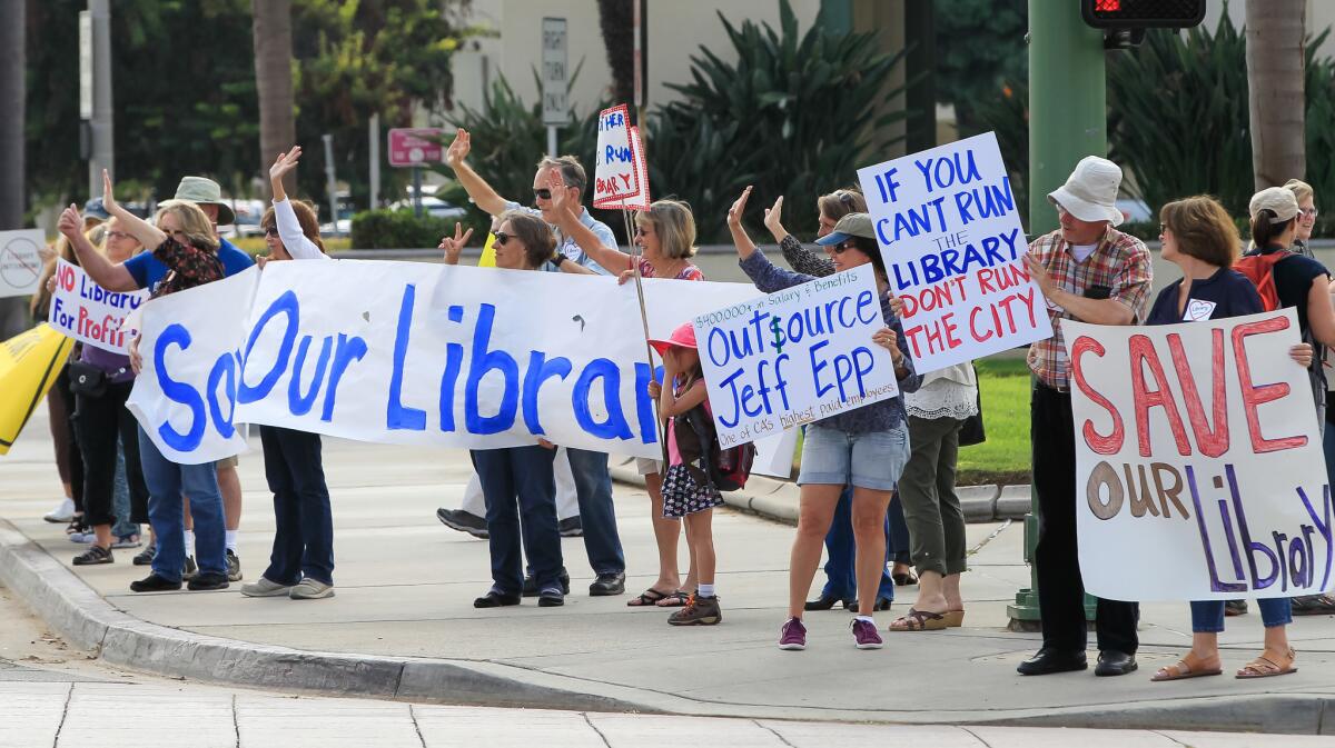 People opposing the plan to outsource library services hold up signs and wave to traffic outside Escondido City Hall before a council meeting August