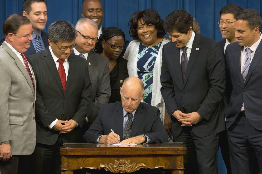 As lawmakers and supporters look on, Gov. Jerry Brown signs legislation that will automatically enroll millions of private-sector workers in retirement saving accounts.