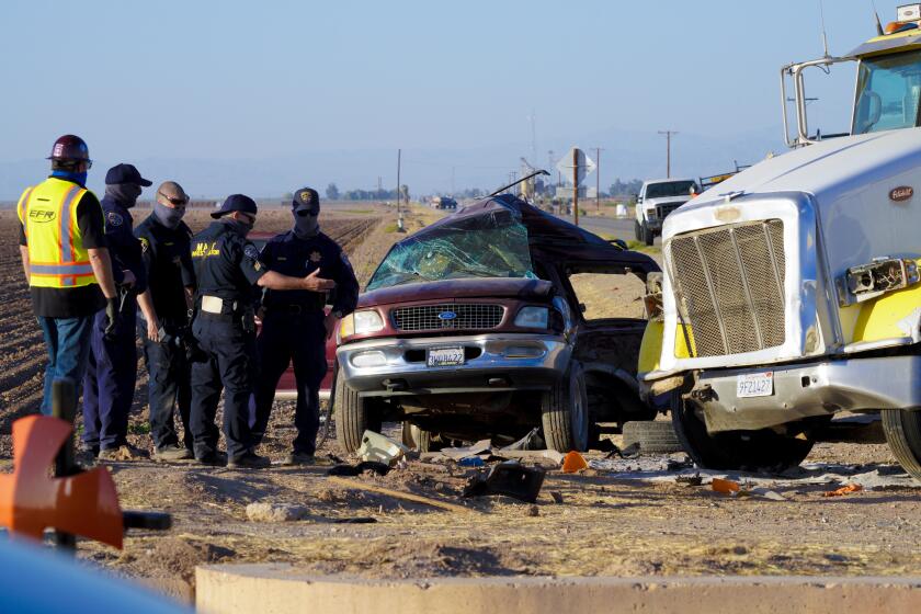 Holtville, CA - March 02: On Tuesday, March 2, 2021 in Holtville, CA., law enforcement investigator look over the SUV after tow wreckers separated it from the and large tractor trailer. The accident was the scene of a deadly crash on State Highway115 near the U.S.-Mexico border. The crash Tuesday morning left at least 13 people dead and several others injured. (Nelvin C. Cepeda / The San Diego Union-Tribune)