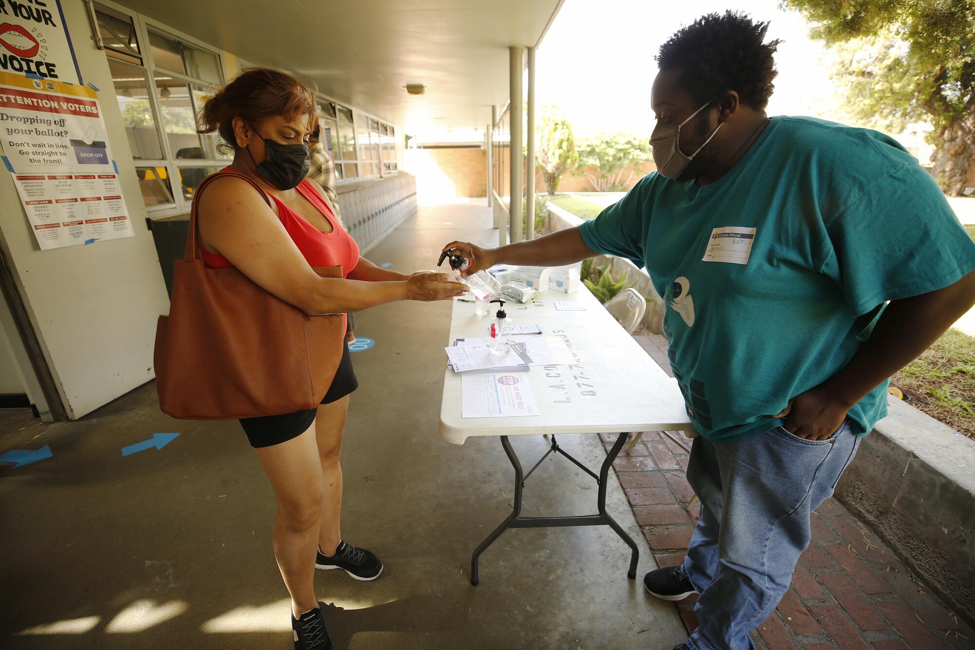 A poll worker squirts hand sanitizer onto a voter's hand