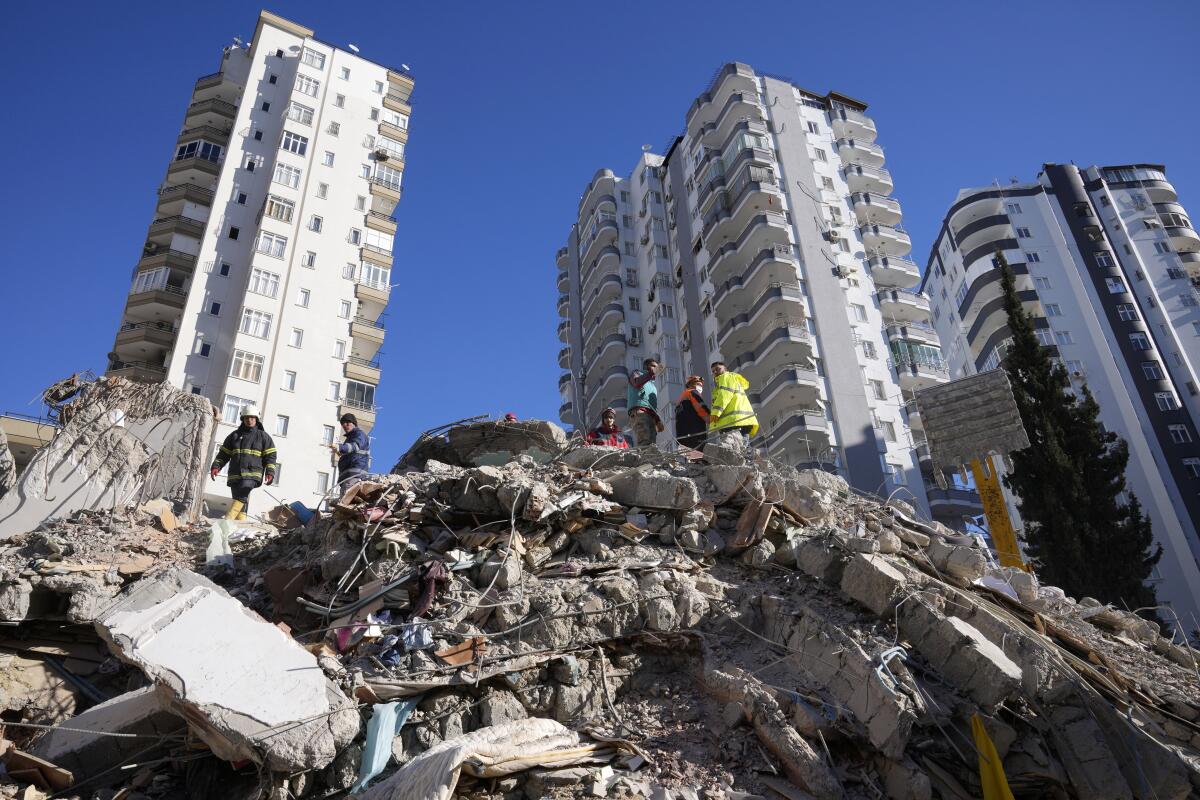 Emergency teams search for survivors amid the rubble of a building in front of other standing tall buildings
