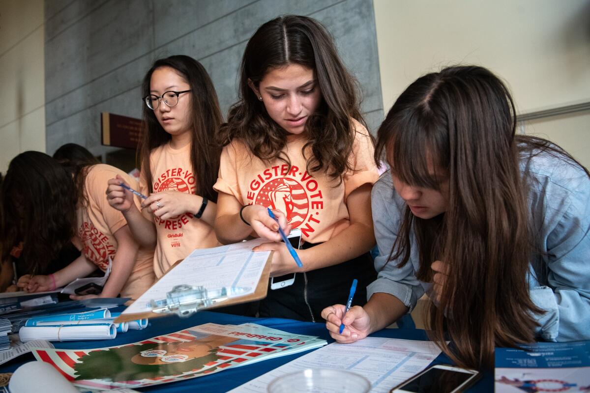 Students fill out voter registration forms at a table.